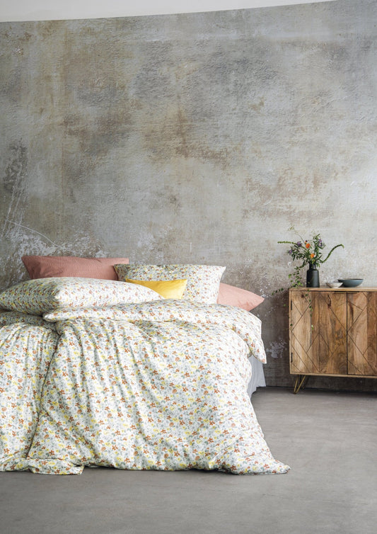 Auf einem Bett liegen mehrere Kopfkissen und eine Bettdecke bezogen mit Soft Seersucker Bettwaesche aus 100 Prozent Baumwolle mit Muster aus Blumen in der Farbe Gelb. Modell Shadow Multi.