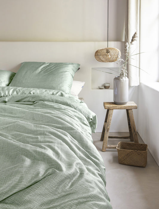 Auf einem Bett liegen mehrere Kopfkissen und eine Bettdecke bezogen mit Tencel-Lyocell Bettwaesche aus 100 Prozent Baumwolle mit Muster aus graphischen Formen in der Farbe Gruen. Modell Lotus Green Line.