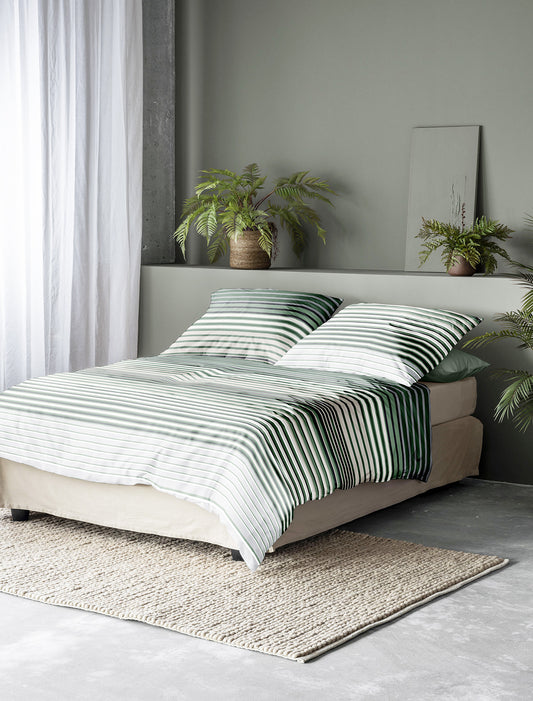 Auf einem Bett liegen mehrere Kopfkissen und eine Bettdecke bezogen mit Tencel-Lyocell Bettwaesche aus 100 Prozent Baumwolle mit Muster aus horizontalen Streifen in der Farbe Gruen. Modell Lotus Green Line.