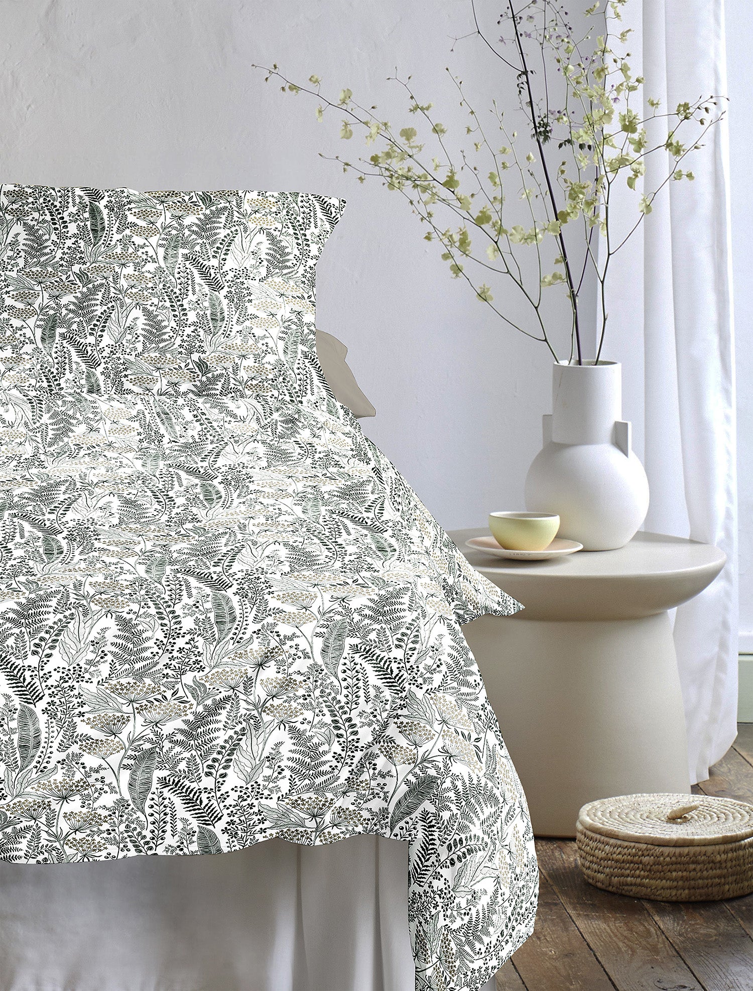Auf einem Bett liegen mehrere Kopfkissen und eine Bettdecke bezogen mit Tencel-Lyocell Bettwaesche aus 100 Prozent Baumwolle mit Muster aus Blaettern in der Farbe Gruen. Modell Lotus Natur.