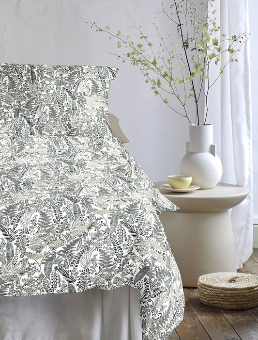 Auf einem Bett liegen mehrere Kopfkissen und eine Bettdecke bezogen mit Tencel-Lyocell Bettwaesche aus 100 Prozent Baumwolle mit Muster aus Blaettern in der Farbe Gruen. Modell Lotus Natur.
