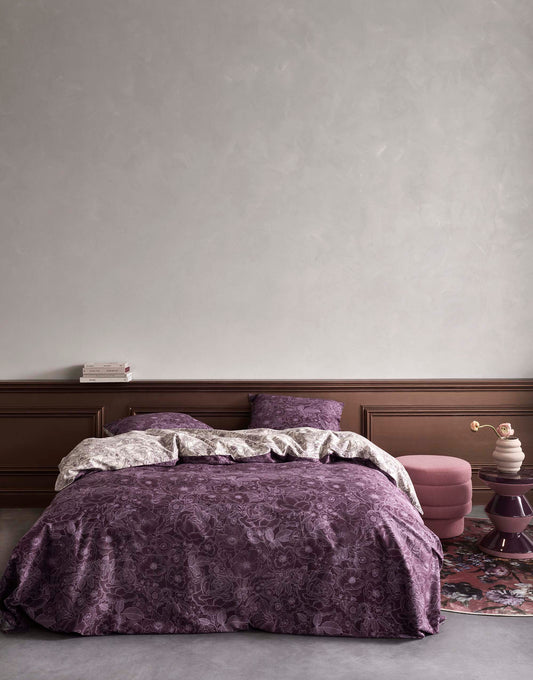 Ein Bettbezug-Set aus mehreren Kopfkissen und einer Bettdecke bezogen mit Twill-Baumwoll Bettwaesche aus 100 Prozent Baumwolle mit Muster aus Rosen in der Farbe Lila. Modell Camille Plum Wine.