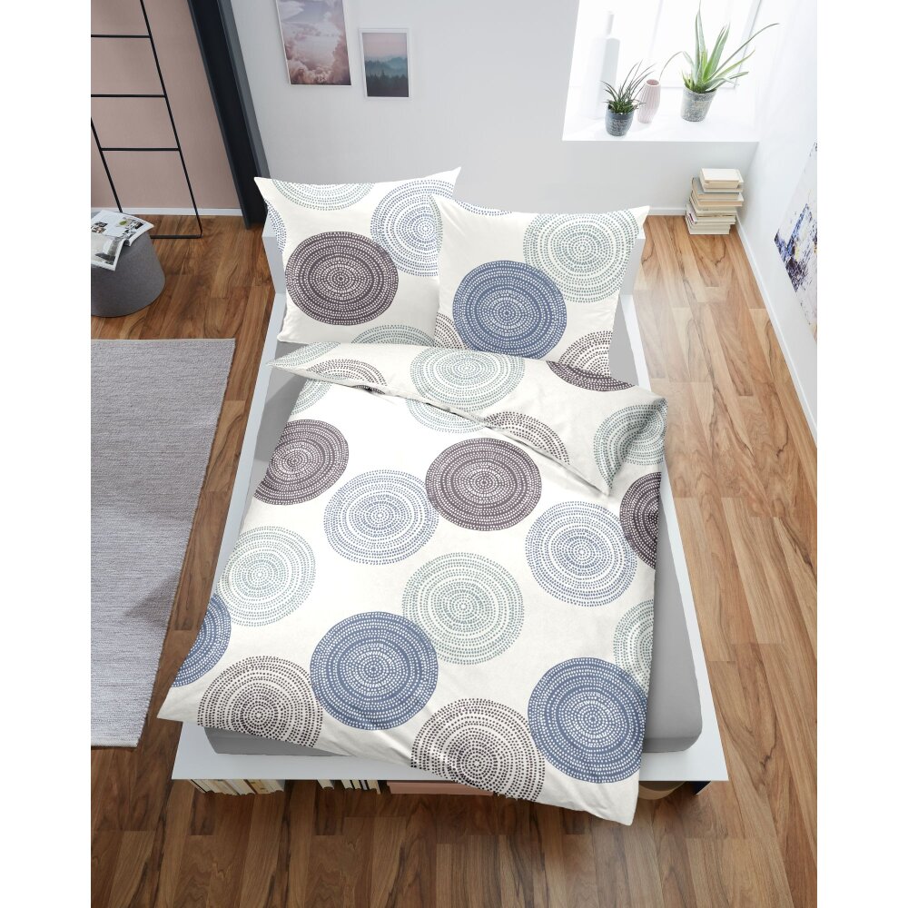 Auf einem Bett liegt ein Kopfkissen und eine Bettdecke bezogen mit Edel-Biber Bettwaesche aus 100 Prozent Baumwolle mit Illustrationen von gepunkteten Kreisen in der Farbe Weiss. Modell Hazy Shades
