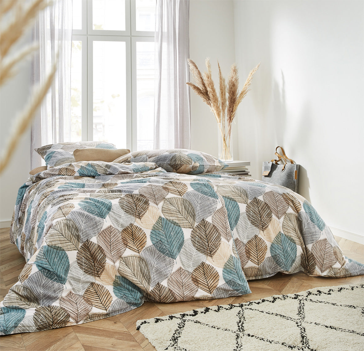 Auf einem Bett liegen mehrere Kopfkissen und eine Bettdecke bezogen mit Edel-Feinbiber Bettwaesche aus 100 Prozent Baumwolle mit Muster aus Blaettern in der Farbe Mehrfarbig. Modell Koala.