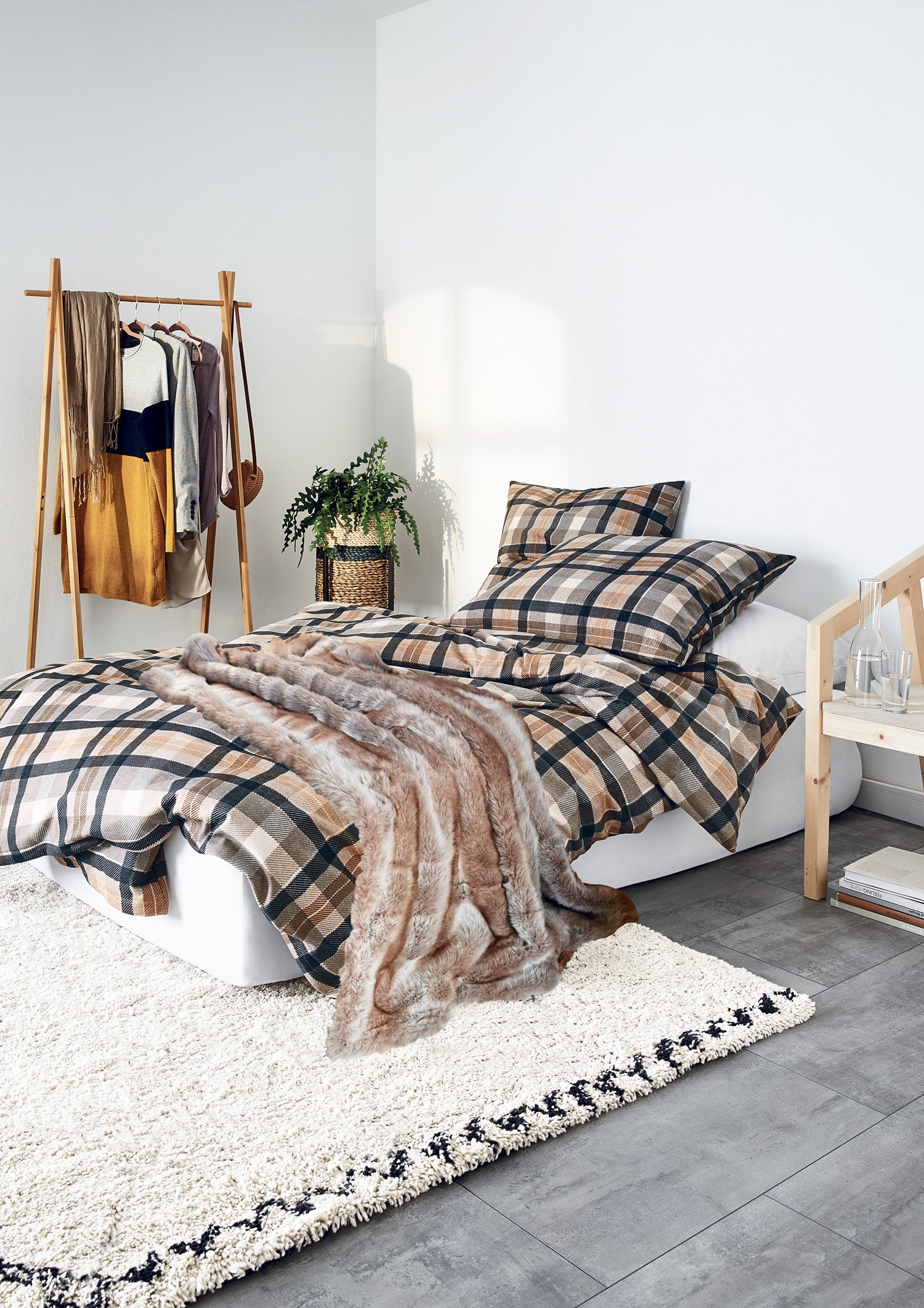 Auf einem Bett liegen mehrere Kopfkissen und eine Bettdecke bezogen mit Edel-Feinbiber Bettwaesche aus 100 Prozent Baumwolle mit Muster aus Quadraten in der Farbe Braun. Modell Koala Natur.
