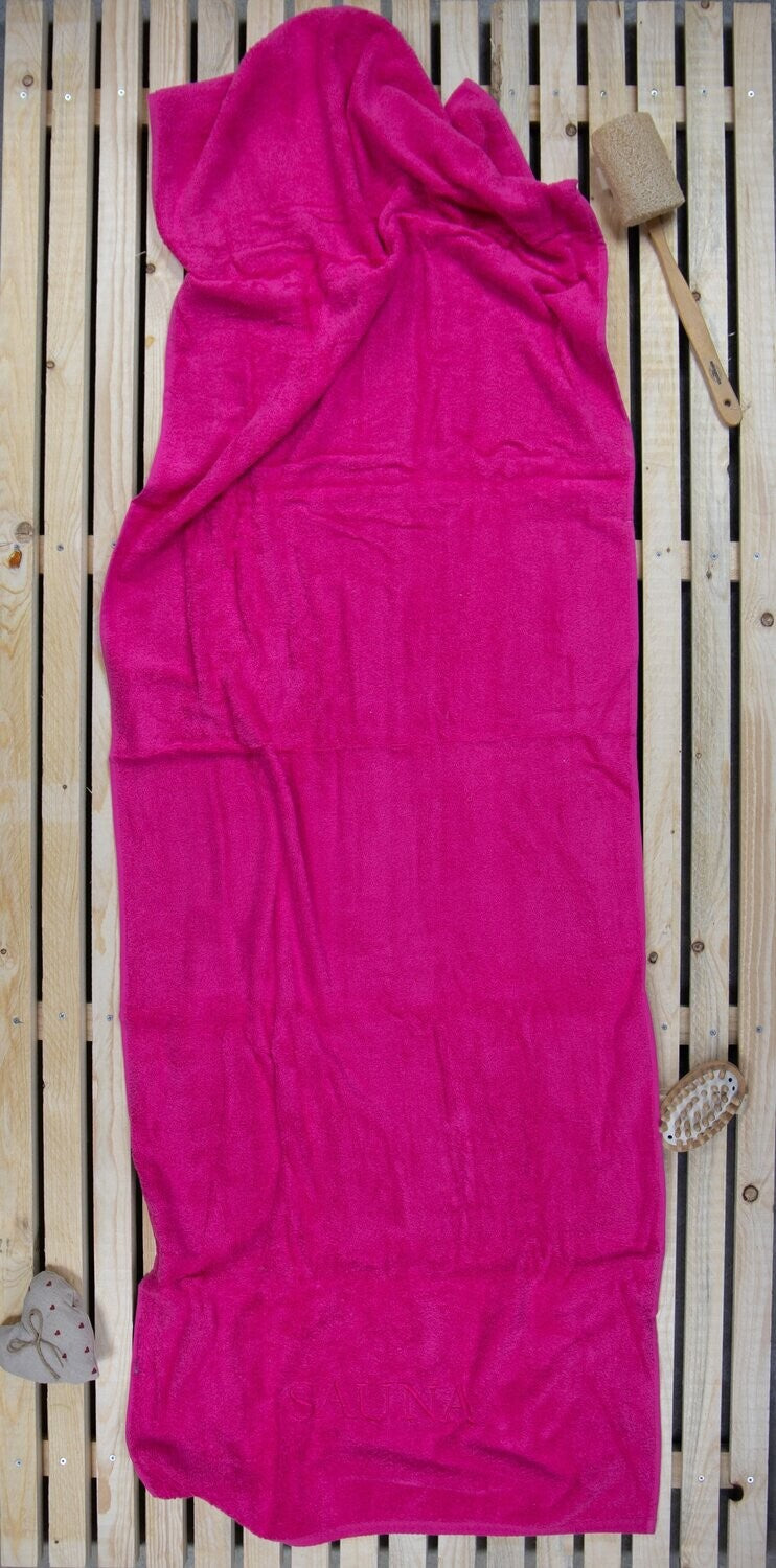 Auf einer Holzbankank liegt ein Saunatuch mit aufgesticktem Text SAUNA von p.k. aus 100 Prozent Baumwolle in der Groesse 70x200cm. Farbe Pink. Modell Pink.