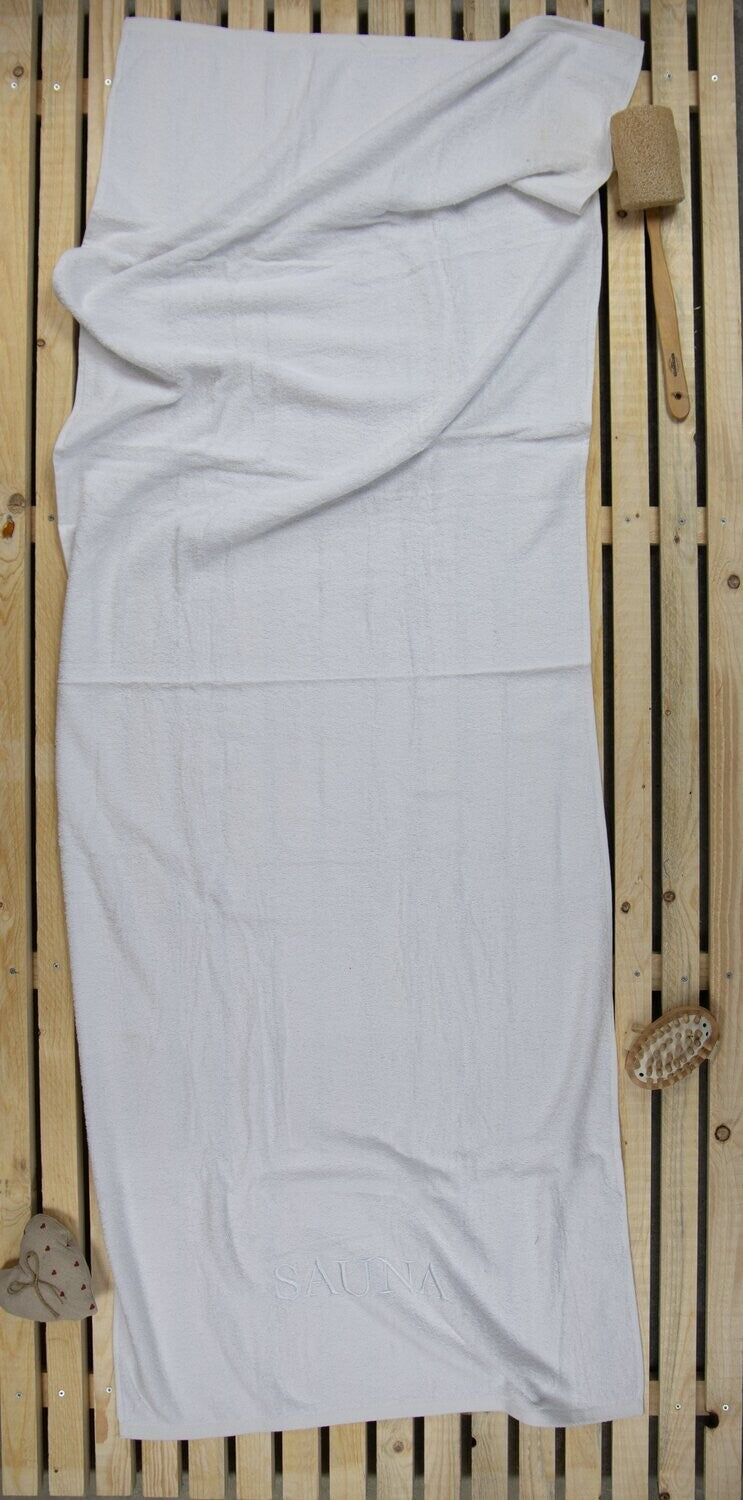 Auf einer Holzbankank liegt ein Saunatuch mit aufgesticktem Text SAUNA von p.k. aus 100 Prozent Baumwolle in der Groesse 70x200cm. Farbe Weiss. Modell Weiss.