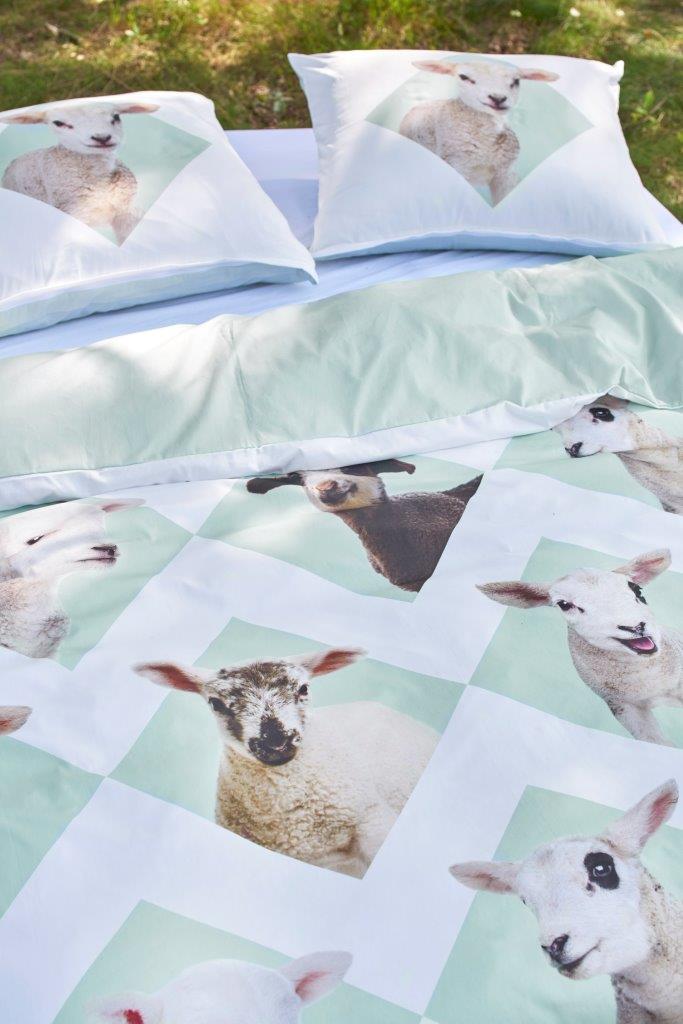 Ein Bett mit mehreren Kopfkissen und einer Bettdecke bezogen mit kuscheliger Covers & Co Bettwaesche aus 100 Prozent Baumwolle mit Illustrationen von Schafen in der Farbe Weiss. Modell Lamsy.