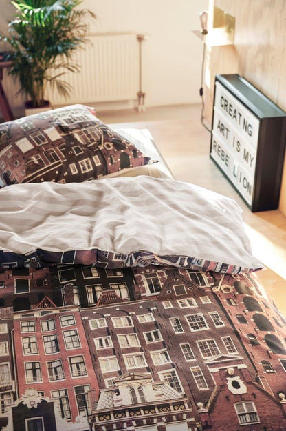 In einem Kinderzimmer steht ein Bett mit einem Kopfkissen und einer Bettdecke bezogen mit kuscheliger Covers & Co Bettwaesche aus 100 Prozent Baumwolle mit Illustrationen von Haeusern in der Farbe Braun. Modell Streets.