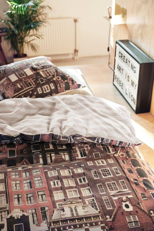 In einem Kinderzimmer steht ein Bett mit einem Kopfkissen und einer Bettdecke bezogen mit kuscheliger Covers & Co Bettwaesche aus 100 Prozent Baumwolle mit Illustrationen von Haeusern in der Farbe Braun. Modell Streets.