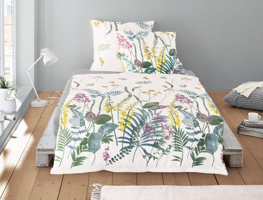 Auf einem Bett liegen mehrere Kopfkissen und eine Bettdecke bezogen mit Mako-Satin Bettwaesche aus 100 Prozent Baumwolle mit Muster aus Blaettern in der Farbe Weiss. Modell Fruehling Weiss.
