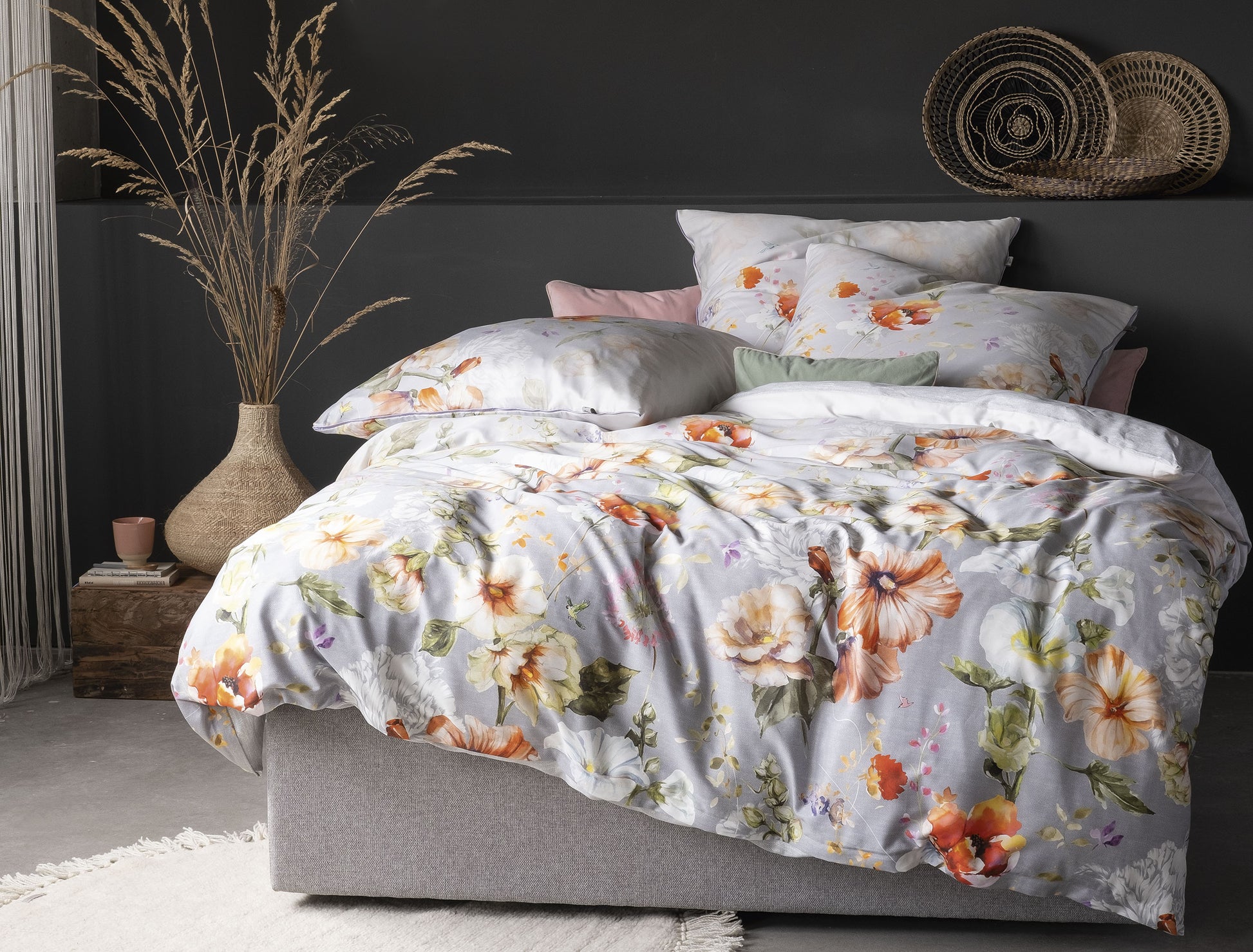 Auf einem Bett liegen mehrere Kopfkissen und eine Bettdecke bezogen mit Mako-Satin Bettwaesche aus 100 Prozent Baumwolle mit Muster aus Blumen in der Farbe Silber. Modell Magic.