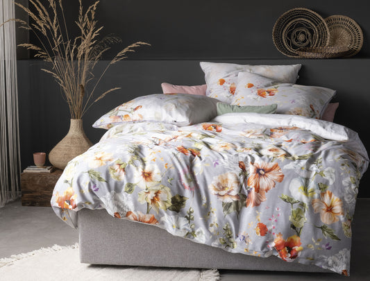Auf einem Bett liegen mehrere Kopfkissen und eine Bettdecke bezogen mit Mako-Satin Bettwaesche aus 100 Prozent Baumwolle mit Muster aus Blumen in der Farbe Silber. Modell Magic.
