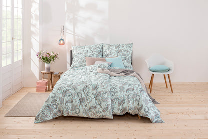 Ein Bettbezug-Set aus mehreren Kopfkissen und einer Bettdecke bezogen mit Mako-Interlock-Jersey Bettwaesche aus 100 Prozent Baumwolle mit Muster aus Ornamenten in der Farbe Blau. Modell Paisley hellblau.