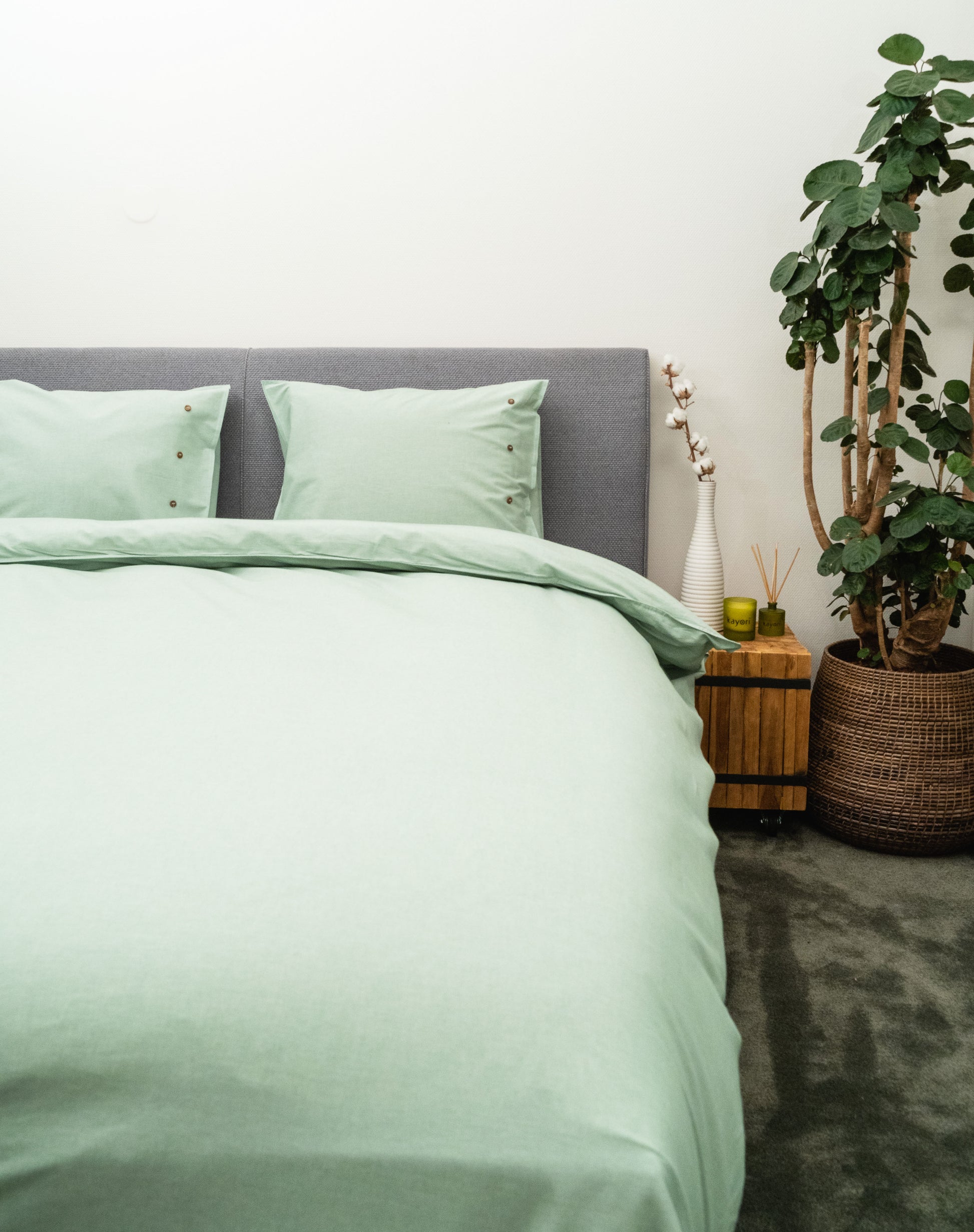 Auf einem Bett liegen mehrere Kopfkissen und eine Bettdecke bezogen mit Perkal-Baumwoll Bettwaesche aus 100 Prozent Baumwolle in der Farbe Gruen. Modell Gruen.