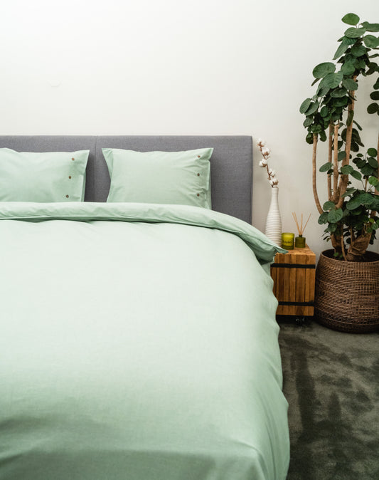 Auf einem Bett liegen mehrere Kopfkissen und eine Bettdecke bezogen mit Perkal-Baumwoll Bettwaesche aus 100 Prozent Baumwolle in der Farbe Gruen. Modell Gruen.
