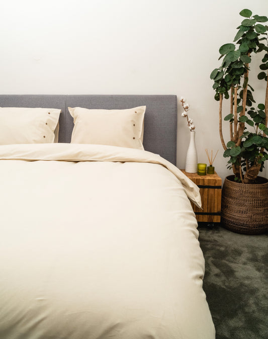 Auf einem Bett liegen mehrere Kopfkissen und eine Bettdecke bezogen mit Perkal-Baumwoll Bettwaesche aus 100 Prozent Baumwolle in der Farbe Beige. Modell Natur.