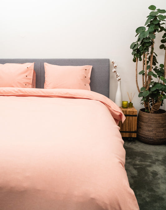 Auf einem Bett liegen mehrere Kopfkissen und eine Bettdecke bezogen mit Perkal-Baumwoll Bettwaesche aus 100 Prozent Baumwolle in der Farbe Orange. Modell Orange.