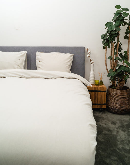 Auf einem Bett liegen mehrere Kopfkissen und eine Bettdecke bezogen mit Perkal-Baumwoll Bettwaesche aus 100 Prozent Baumwolle in der Farbe Silber. Modell Silbergrau.
