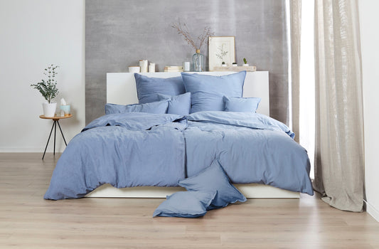 Auf einem Bett liegen mehrere Kopfkissen und eine Bettdecke bezogen mit Renforce Bettwaesche aus 100 Prozent Baumwolle in der Farbe Blau. Modell Stone-Washed Blau 365.