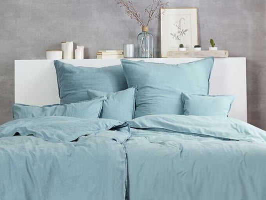 Auf einem Bett liegen mehrere Kopfkissen und eine Bettdecke bezogen mit Renforce Bettwaesche aus 100 Prozent Baumwolle in der Farbe Gruen. Modell Stone-Washed Gruen 588.