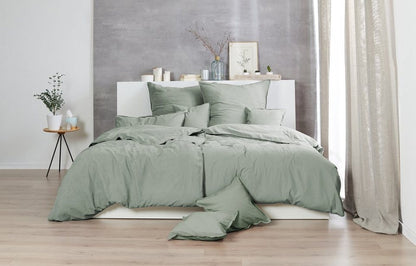 Auf einem Bett liegen mehrere Kopfkissen und eine Bettdecke bezogen mit Renforce Bettwaesche aus 100 Prozent Baumwolle in der Farbe Gruen. Modell Stone-Washed Olive 518.