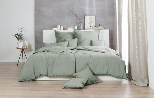 Auf einem Bett liegen mehrere Kopfkissen und eine Bettdecke bezogen mit Renforce Bettwaesche aus 100 Prozent Baumwolle in der Farbe Gruen. Modell Stone-Washed Olive 518.