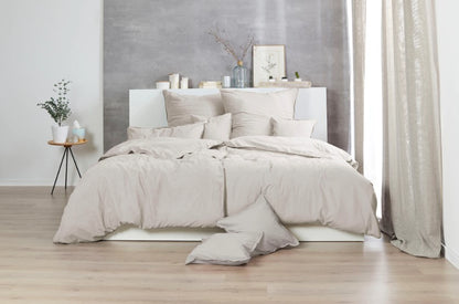 Auf einem Bett liegen mehrere Kopfkissen und eine Bettdecke bezogen mit Renforce Bettwaesche aus 100 Prozent Baumwolle in der Farbe Beige. Modell Stone-Washed Sand 719.