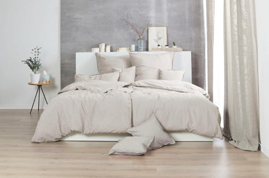 Auf einem Bett liegen mehrere Kopfkissen und eine Bettdecke bezogen mit Renforce Bettwaesche aus 100 Prozent Baumwolle in der Farbe Beige. Modell Stone-Washed Sand 719.