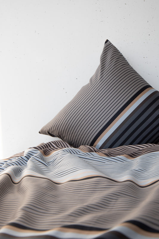 Ein Kopfkissen und eine Bettdecke bezogen mit seidig-weicher Satin Bettwaesche von Casatex mit einem Streifenmuster in der Farbe Grau. Modell Grey Stripe.