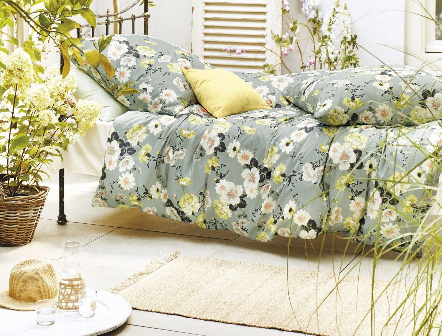 Auf einem Bett liegen mehrere Kopfkissen und eine Bettdecke bezogen mit Satin Bettwaesche aus 100 Prozent Baumwolle mit Muster aus Blumen in der Farbe Mint. Modell Blumen Mint.