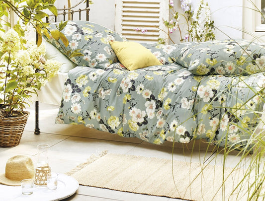 Auf einem Bett liegen mehrere Kopfkissen und eine Bettdecke bezogen mit Satin Bettwaesche aus 100 Prozent Baumwolle mit Muster aus Blumen in der Farbe Mint. Modell Blumen Mint.