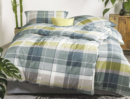 Auf einem Bett liegen mehrere Kopfkissen und eine Bettdecke bezogen mit Satin Bettwaesche aus 100 Prozent Baumwolle mit Muster aus Quadraten in der Farbe Gruen. Modell Karo Gruen.