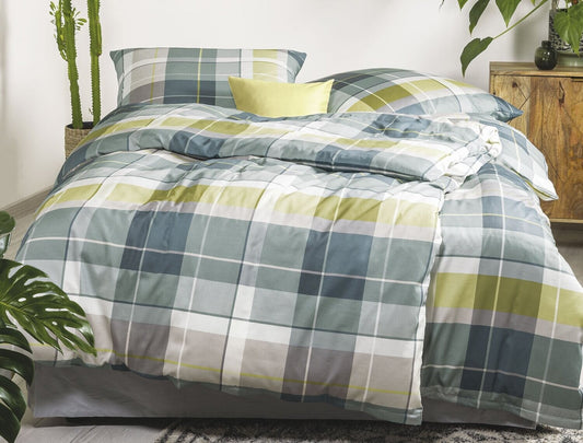 Auf einem Bett liegen mehrere Kopfkissen und eine Bettdecke bezogen mit Satin Bettwaesche aus 100 Prozent Baumwolle mit Muster aus Quadraten in der Farbe Gruen. Modell Karo Gruen.