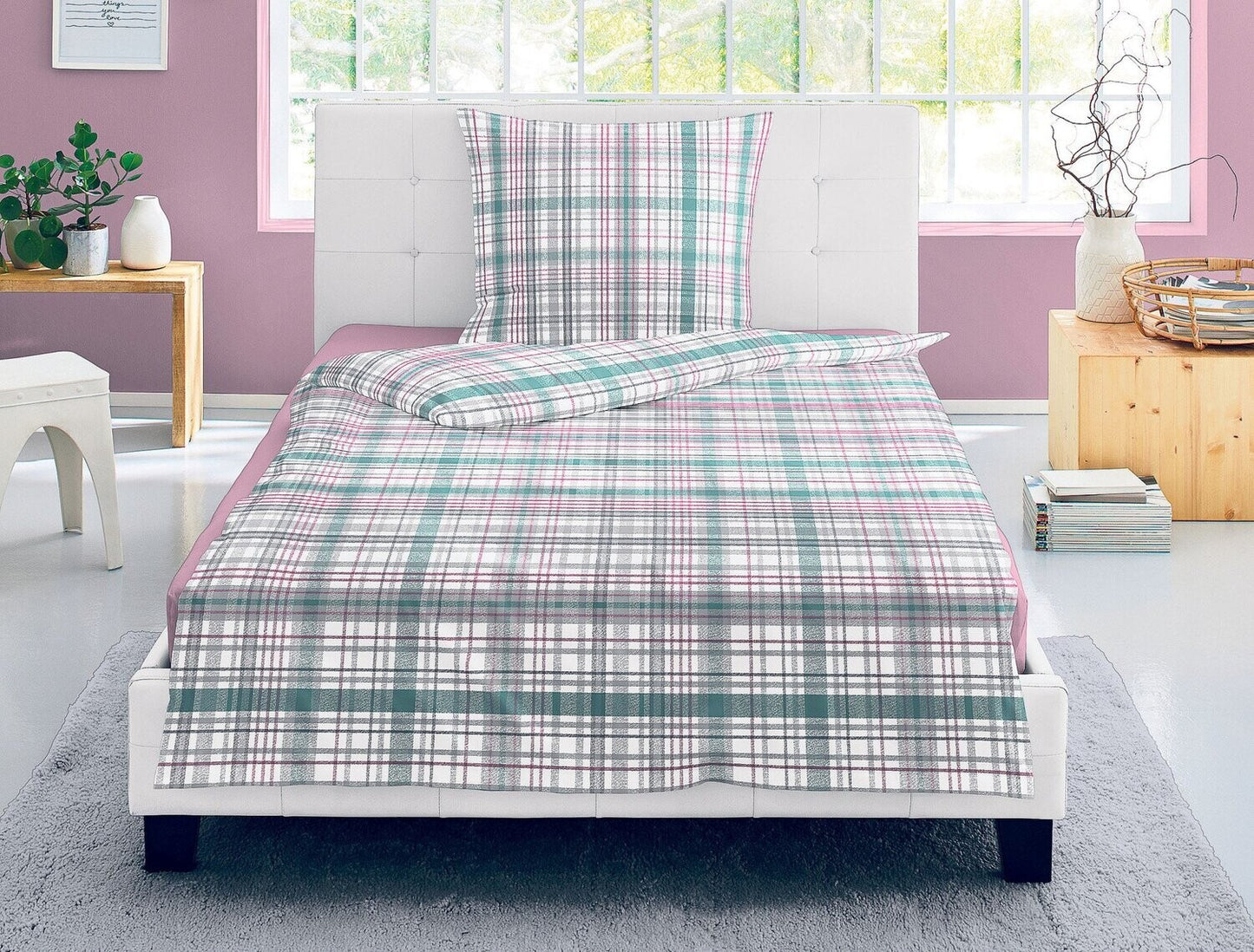 Auf einem Bett liegen mehrere Kopfkissen und eine Bettdecke bezogen mit Satin Bettwaesche aus 100 Prozent Baumwolle mit Muster aus Quadraten in der Farbe Rosa. Modell Karo Rosa Gruen.
