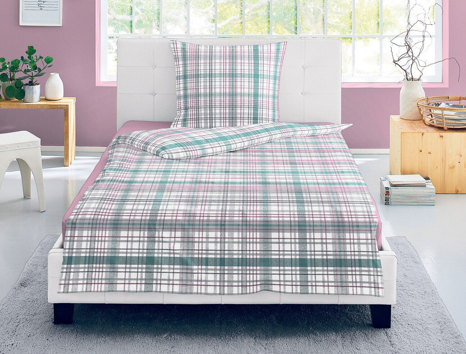Auf einem Bett liegen mehrere Kopfkissen und eine Bettdecke bezogen mit Satin Bettwaesche aus 100 Prozent Baumwolle mit Muster aus Quadraten in der Farbe Rosa. Modell Karo Rosa Gruen.