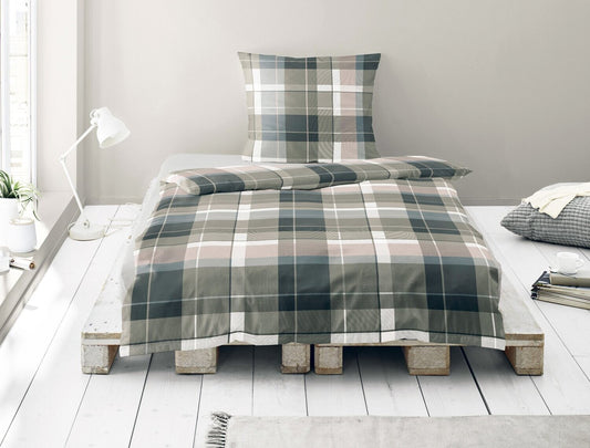 Auf einem Bett liegen mehrere Kopfkissen und eine Bettdecke bezogen mit Satin Bettwaesche aus 100 Prozent Baumwolle mit Muster aus Quadraten in der Farbe Grau. Modell Karo Rosenholz.