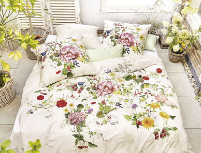 Auf einem Bett liegen mehrere Kopfkissen und eine Bettdecke bezogen mit Satin Bettwaesche aus 100 Prozent Baumwolle mit Muster aus Blumen in der Farbe Weiss. Modell Rose Weiss.