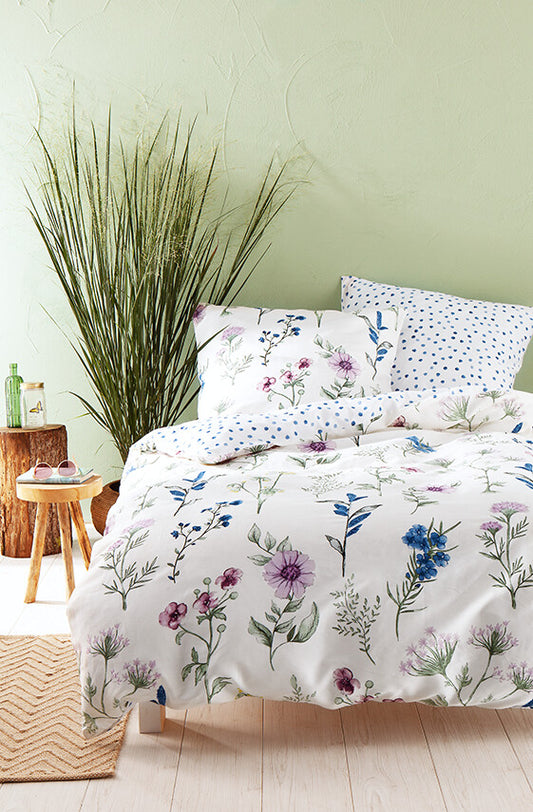 Auf einem Bett liegen mehrere Kopfkissen und eine Bettdecke bezogen mit Satin Bettwaesche aus 100 Prozent Baumwolle mit Muster aus Blumen und Punkten  in der Farbe Weiss. Modell Blumen Punkte.