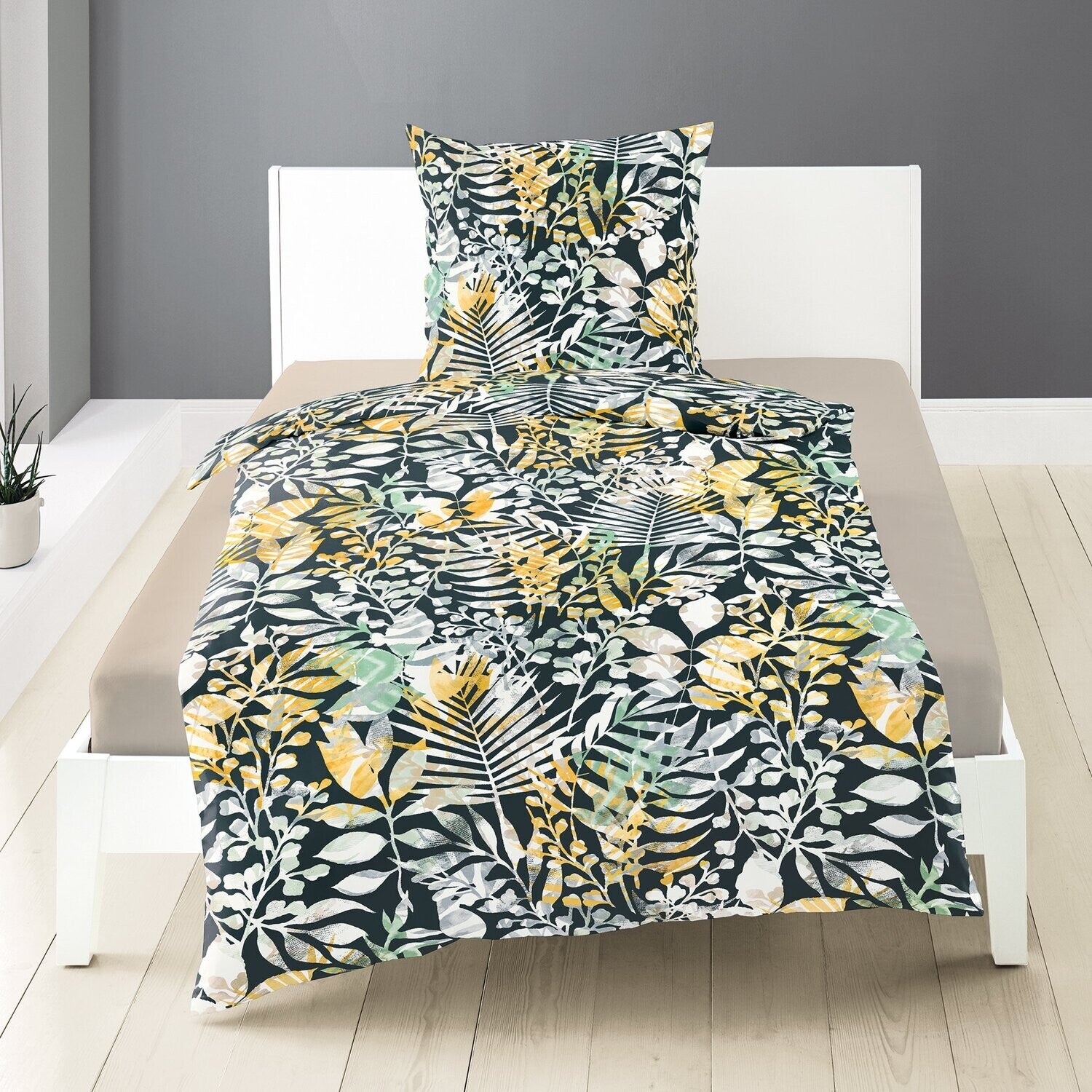 Auf einem Bett liegen mehrere Kopfkissen und eine Bettdecke bezogen mit Satin Bettwaesche aus 100 Prozent Baumwolle mit Muster aus Blaettern in der Farbe Mehrfarbig. Modell Leaves.