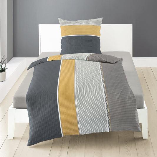 Auf einem Bett liegen mehrere Kopfkissen und eine Bettdecke bezogen mit Satin Bettwaesche aus 100 Prozent Baumwolle mit Muster aus grafischen Formen in der Farbe Grau. Modell Stripe.