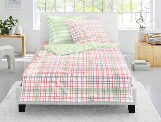 Auf einem Bett liegen mehrere Kopfkissen und eine Bettdecke bezogen mit Satin Bettwaesche aus 100 Prozent Baumwolle mit Muster aus Quadraten in der Farbe Rosa. Modell Karo Rosa.