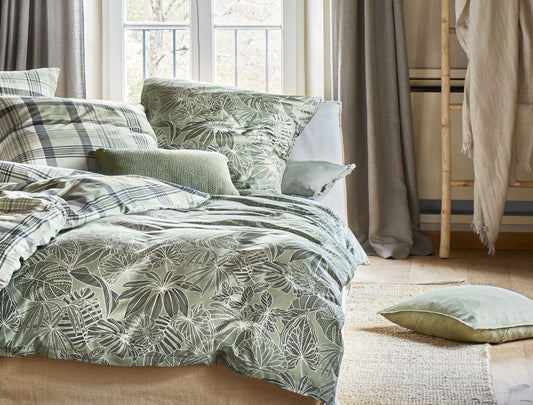 Auf einem Bett liegen mehrere Kopfkissen und eine Bettdecke bezogen mit Soft Seersucker Bettwaesche aus 100 Prozent Baumwolle mit Muster aus Blaettern in der Farbe Gruen. Modell Easy-Plant.