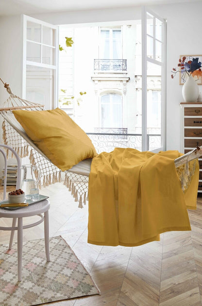 Auf einer Haengematte liegt ein Kopfkissen und ein Sommertuch in der Farbe Gelb. Modell Sommer-Set Mustard.