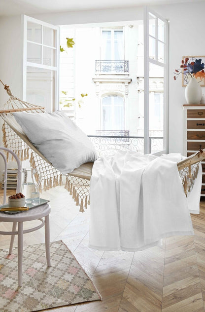 Auf einer Haengematte liegt ein Kopfkissen und ein Sommertuch in der Farbe Weiss. Modell Sommer-Set White.